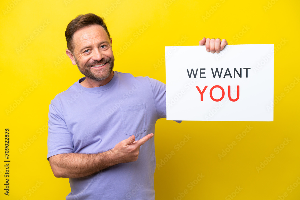 Middle age caucasian man isolated on yellow background holding We Want You board and pointing it Middle age caucasian man isolated on yellow background holding We Want You board and pointing it