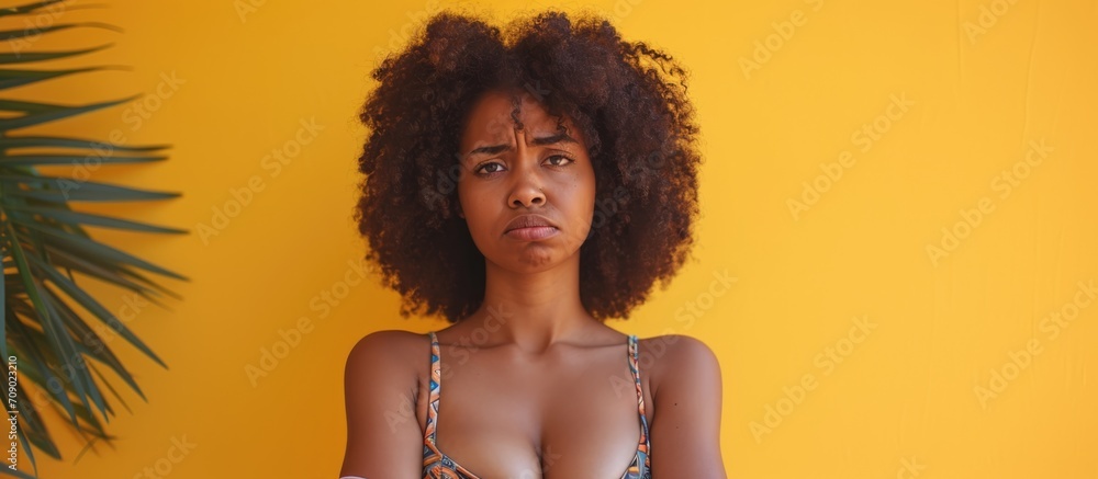 An apprehensive African American woman in a bikini, exhibiting doubt and disapproval with crossed arms. An apprehensive African American woman in a bikini, exhibiting doubt and disapproval with crossed arms.