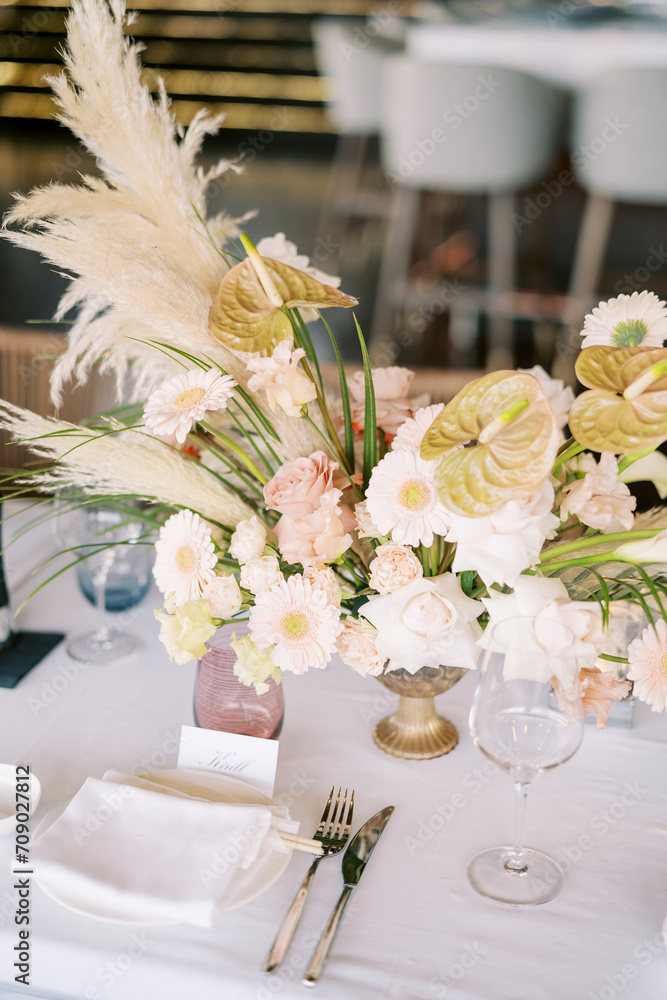 Large bouquet of flowers stands on the festive table near the name card in front of the plate