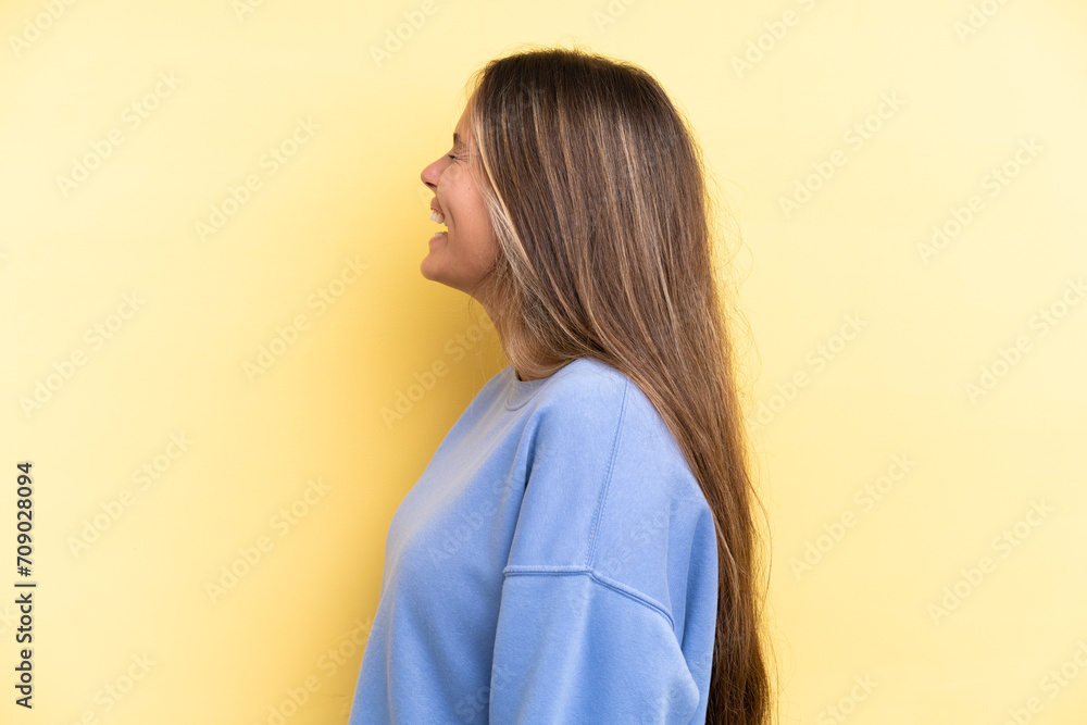 Young caucasian woman isolated on yellow background laughing in lateral position Young caucasian woman isolated on yellow background laughing in lateral position