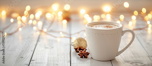 White cup with hot drink on white wooden table with festive lights.