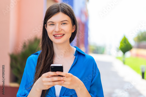 Young pretty woman at outdoors sending a message with the mobile Free Download Young pretty woman at outdoors sending a message with the mobile - GFXLoad