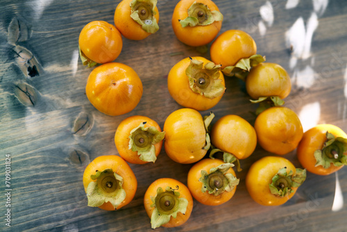 Juicy persimmons lie in bulk on a wooden table under sunlight. Top view