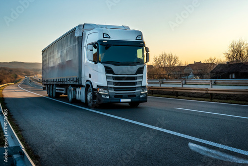 Big semi trailer truck on a highway driving at bright sunny sunset. Transportation vehicle photo
