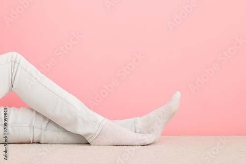Girl long legs in white jeans and socks sitting on light beige carpet at pink wall background. Pastel color. Closeup. Side view. Empty place for text. photo