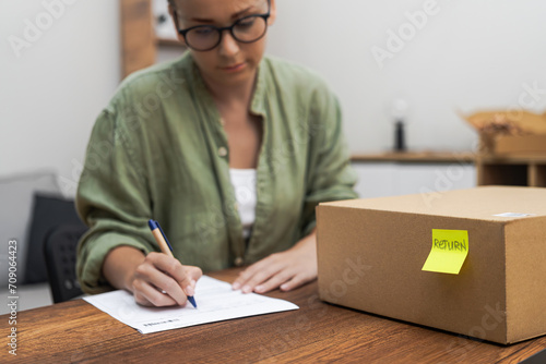 woman writes a return order at home, her determination evident as she fills out the form to return a purchased item.  photo