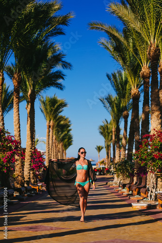 Carefree young woman at an exotic resort among palm trees. A girl in a beautiful swimsuit and glasses. Vacation, spa, and travel concept. © Vladislav