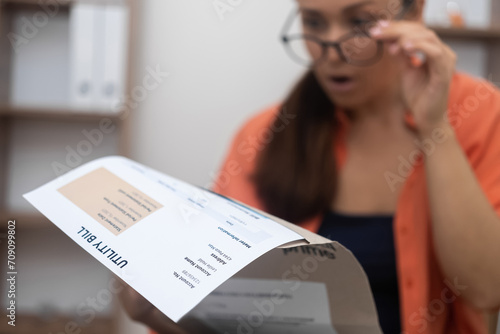 A concerned lady, her face etched with worry, examines a utility bill, apprehensive about mortgage payments and increasing debt. 