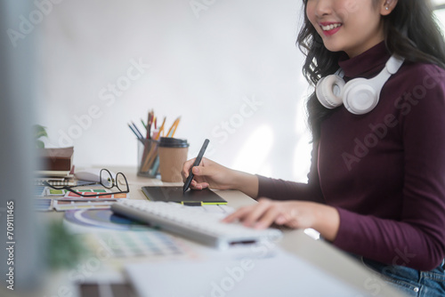 Graphic designer freelance women wear headphone in her neck sketching logo brand on digital tablet and typing on computer while working about graphic design with technology equipment in home studio photo