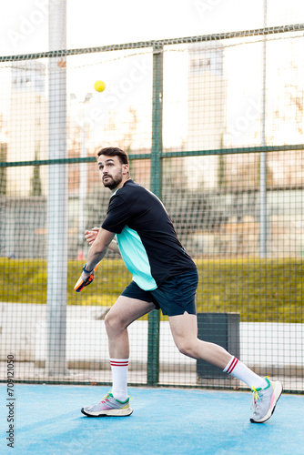Vertical photo of an adult man doing a backhand during a paddle tennis match on an outdoor court. Paddle concept. Young men playing paddle tennis. ©  Yistocking