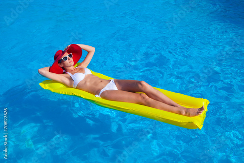 Woman with perfect tanned body lying on yellow air mattress in the pool
