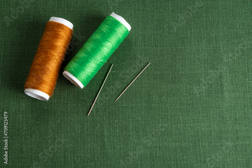Green textile background with spools of thread and needles