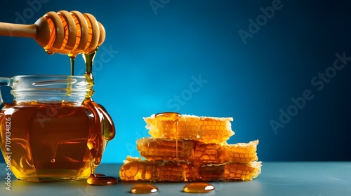 Pouring honey in jar and honeycomb on blue table.