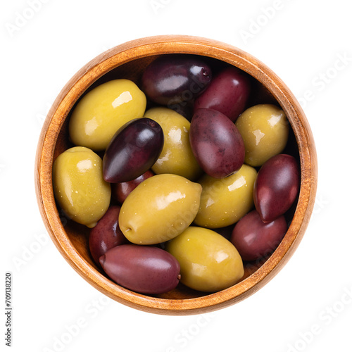 Kalamata and green olives with pit, pickled whole, large Greek table olives, in a wooden bowl. Purple ripe fruits picked when ripe, and green olives picked while still unripe, both preserved in brine.