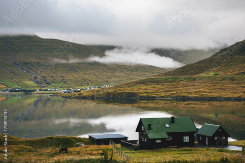 fjordand mountains with reflections in the water with black house in the foreground