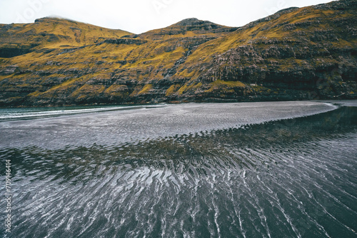 landscape with black shore and sand waves in the faroe islands by the mountains