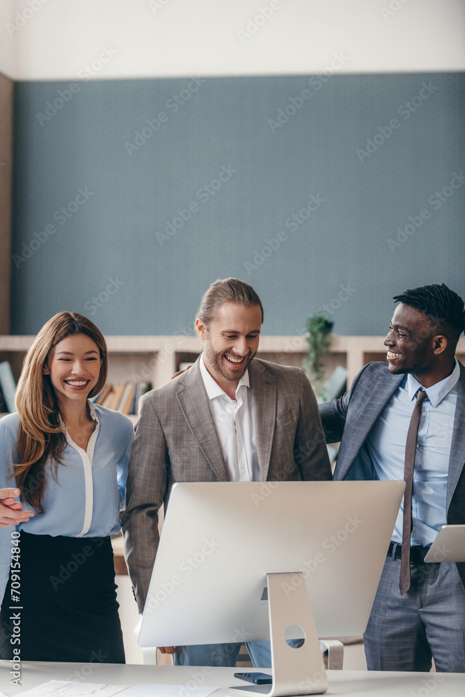 Fototapeta premium Group of business people looking happy while standing near the computer monitor in office together