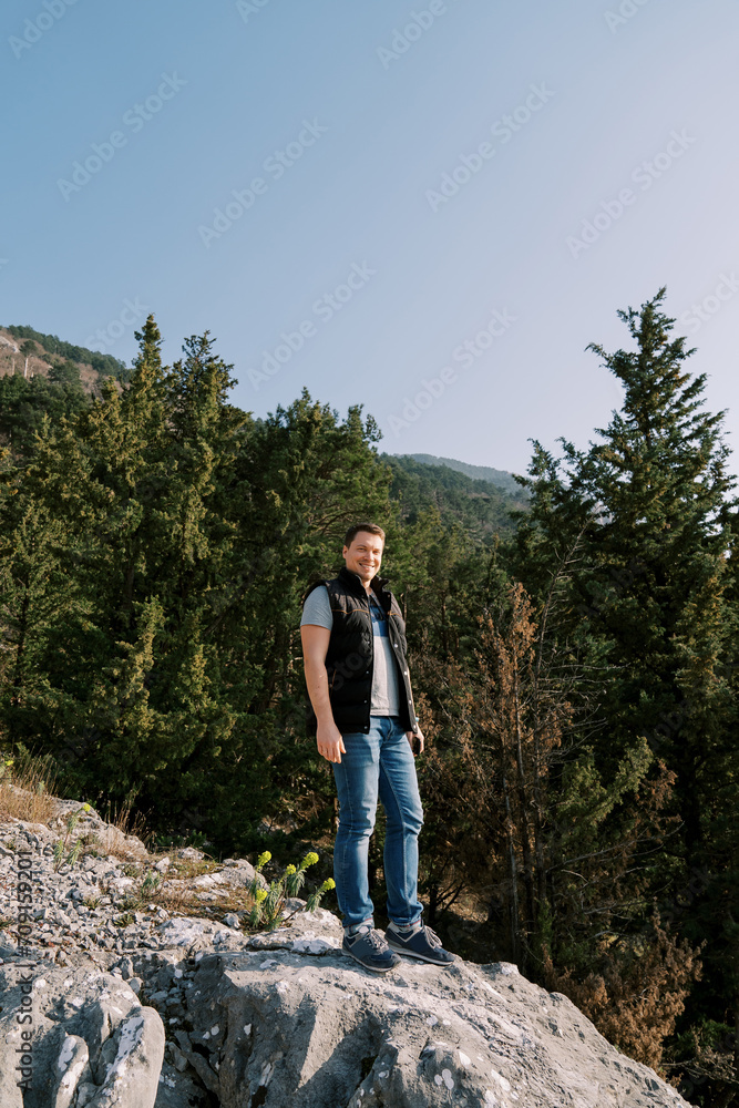 Smiling man stands on a stone hill in the mountains