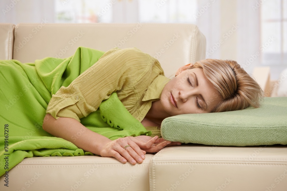Blond woman sleeping with blanket on couch in sunlit living room at home. Blond woman sleeping with blanket on couch in sunlit living room at home.
