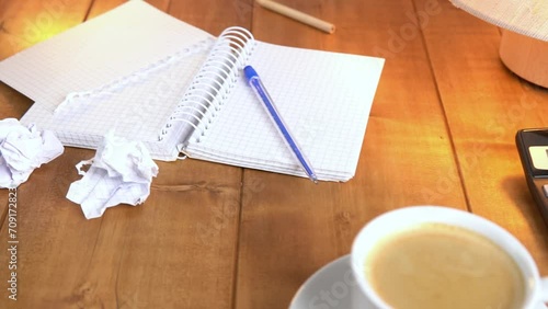 Coffee and a notebook on a brown wooden table under table lamp with warm light, slow motion video.

