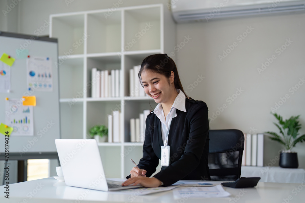 Charming Asian business woman sitting working on laptop in office Charming Asian business woman sitting working on laptop in office