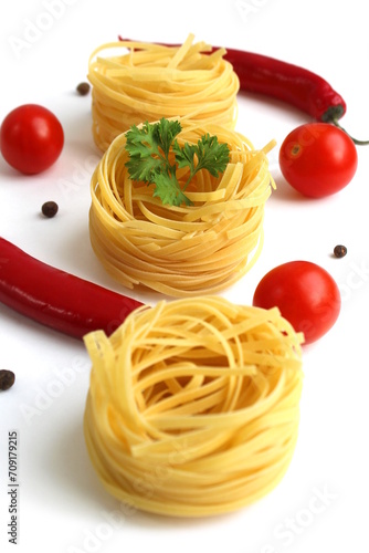 Round spaghetti in the form of a nest with red ripe tomatoes lies on a white background. 