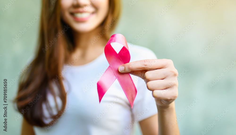 Woman's hand holds pink ribbon, symbolizing breast cancer awareness and medical care Woman's hand holds pink ribbon, symbolizing breast cancer awareness and medical care