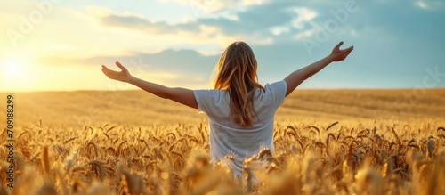 Young woman in wheat field, arms open to the sky, celebrating or meditating.