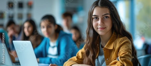 Content college student in computer class, jotting notes while glancing at camera.