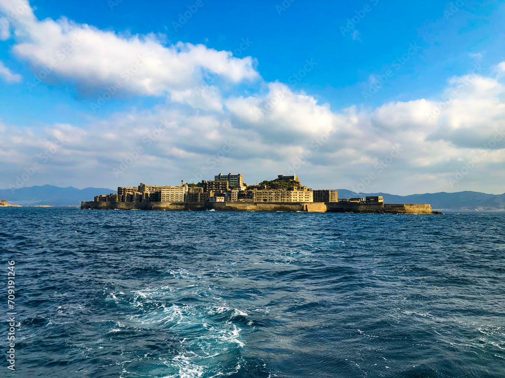 Gunkanjima: A serene seascape encircles the abandoned remnants of Japan's once-thriving Hashima coal mine. Sunlight dances on the waves, framing the island's haunting silhouette.