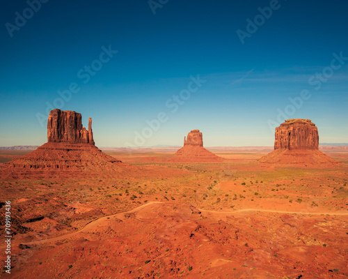 Monument valley landscape  Utah  USA  clear blue sky and long shadows. The three famous mittens  dirt road passing infront.
