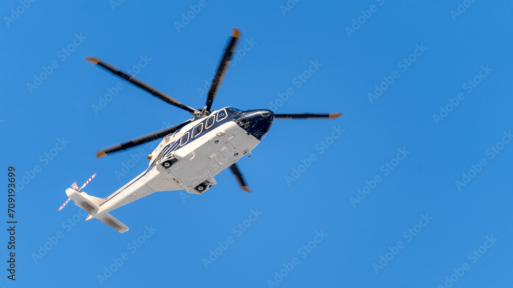 Fototapeta premium White helicopter on blue sky background, Close-up, selective focus, tinted image. Helicopter flight, delivery of passengers by air