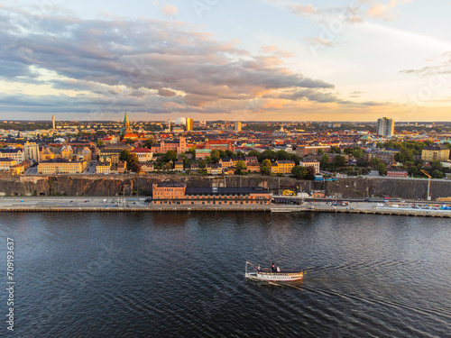 panoramic view over southern Stockholm at sunset, with famous landmarks visible such as the Ericsson Globe. Commuter ferry boat passing by. 