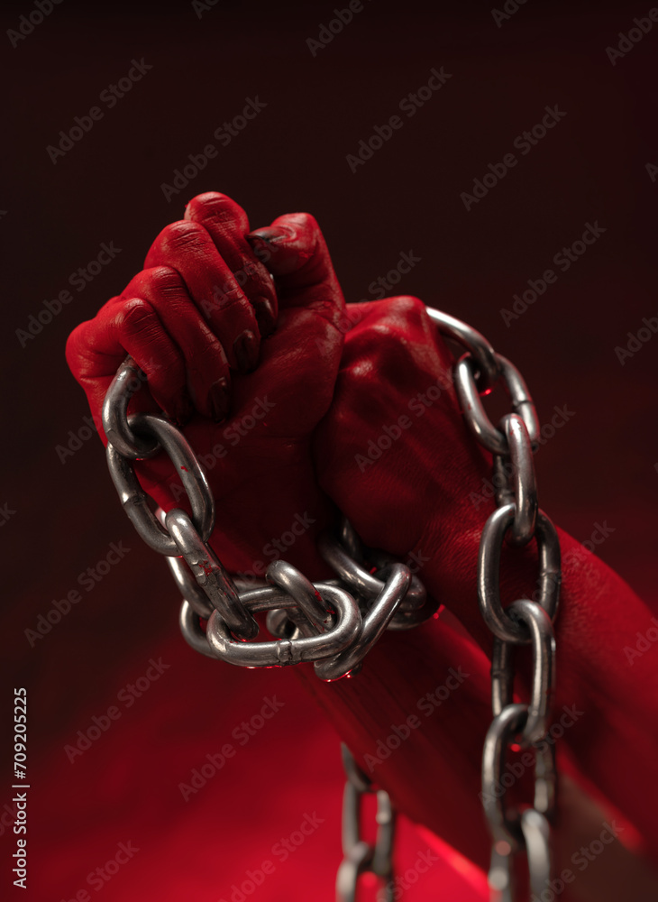bloodied hands clenched into fists in the shackles of a metal chain