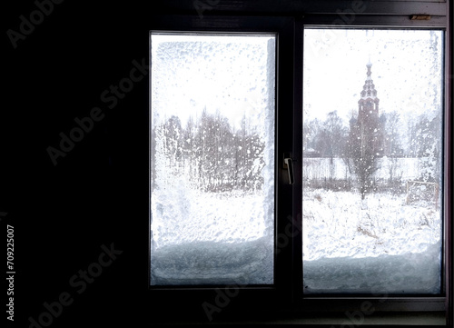 Window in winter with snow and ice on the glass. The silhouette is against the light