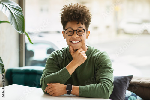 Cheerful african american guy sitting at table next to window photo