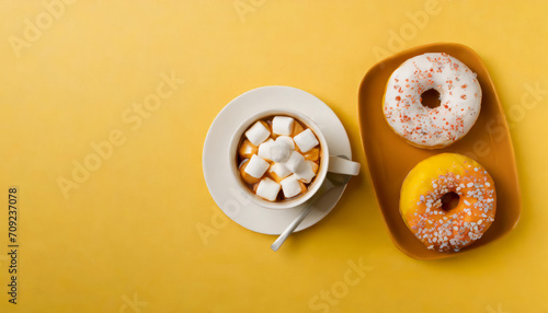 Top view of cup of drink with marshmallow and plate with tasty donuts on yellow background with copy space