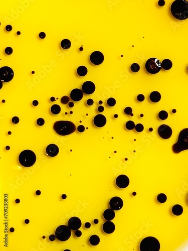 texture of the black bubbles and streaks on yellow background. closeup photo of color ink float on yellow oil. balsamic vinegar in olive oil, italian sauce.