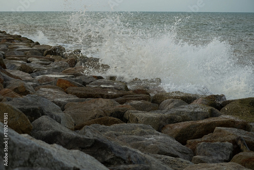 The strong wave hits the rock dam with seascape background