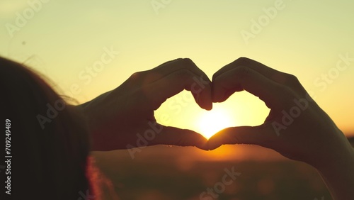 Young woman spends day watching sun set on field. Young woman enjoys incredibly bright sunset creating heart-shaped symbol. Young woman calms down after run in field feeling love with thanksgiving