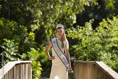 Foto Young, beautiful, blonde woman in white suit, diamond crown and beauty pageant winner's sash, posing in the middle of a wooden bridge