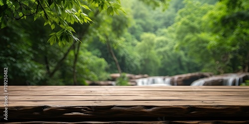 Wooden table top with blurred waterfall and forest background in Thailand's national park. Suitable for product display or design layout. Provides a view with empty space for text.