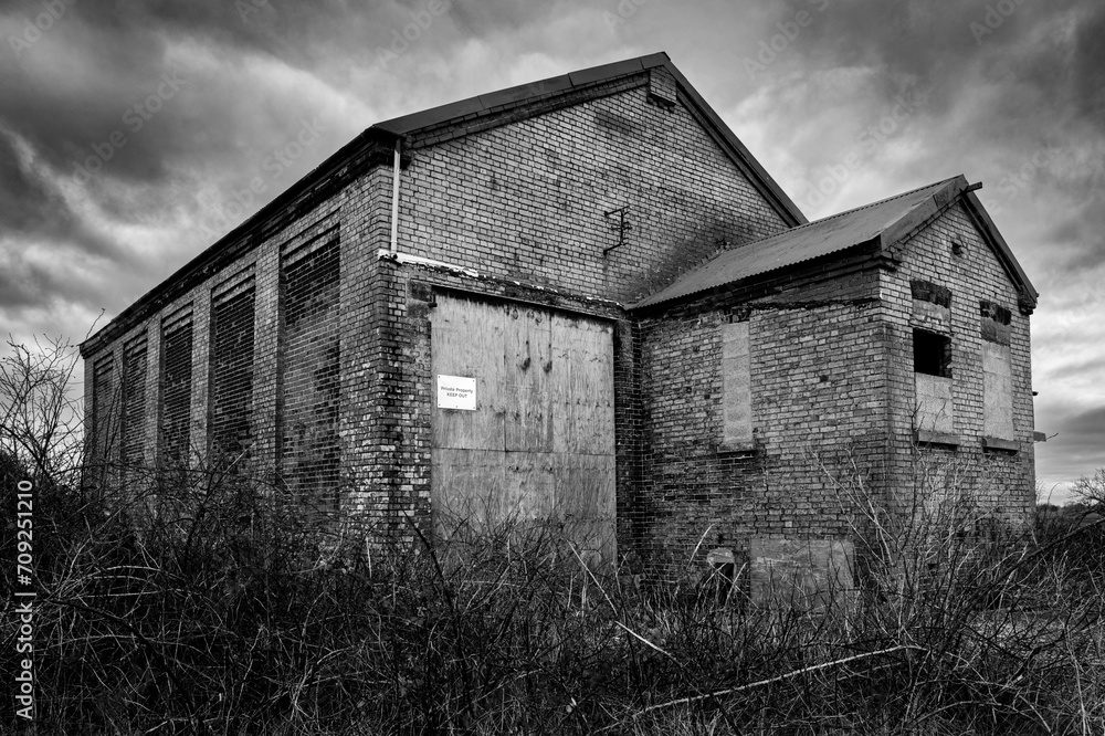 Dramatic view of a long abandoned steam engine maintenance shed seen in rural East Anglia, UK. Seen with the locomotive entrance boarded up with chipboard. Dramatic view of a long abandoned steam engine maintenance shed seen in rural East Anglia, UK. Seen with the locomotive entrance boarded up with chipboard.