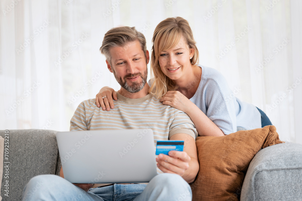 Mature couple sitting at home and using laptop for shopping online