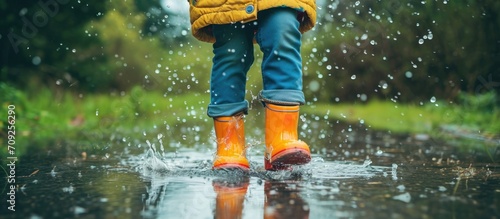 Child wearing rain boots leaps in a puddle. photo