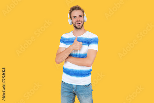 man uses his wireless headphones to listen to music, thumb up. man listen and enjoys live music. man listens to music on his headphones isolated on yellow. man relaxes and listens to music in studio