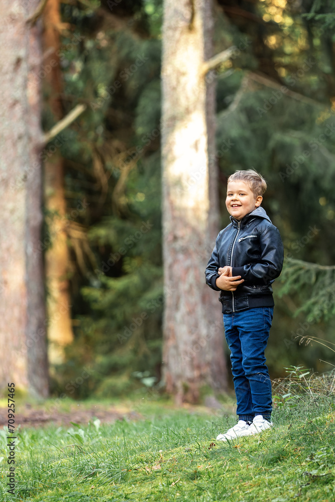 Cheerful smiling boy in forest, he standing near big pine trees and posing