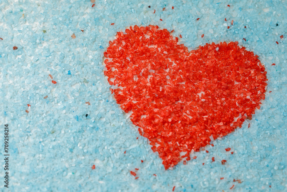 The shape of a red heart on a light blue background is made of colored sand crystals. The shape of a red heart on a light blue background is made of colored sand crystals.