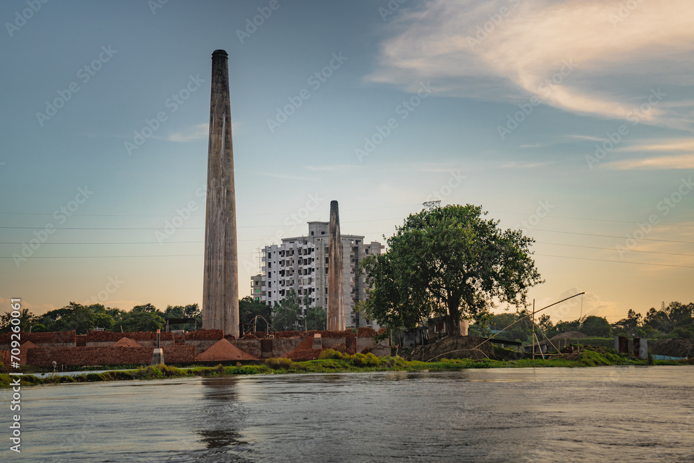 Obraz premium brick chimney, tree, building and clear sky at the bank of the river