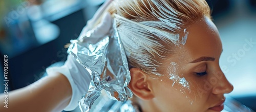 Hairdresser applies bleaching powder on woman's hair and wraps it in foil.
